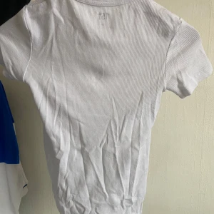Vit ribbad t-shirt från 157 - Säljer en stilren vit ribbad t-shirt från 157 i storlek XS. Perfekt basplagg med korta ärmar och rund halsringning. Passar till alla tillfällen och är lätt att matcha med andra kläder. Skicka ett meddelande vid intresse!