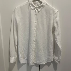 Vit bomulls skjorta från Uniqlo! - Säljer en stilren vit bomulls skjorta från Uniqlo i storlek XS. Skjortan har en klassisk krage och knappar framtill. Perfekt för en minimalistisk look. I perfekt skick, då den endast använts en gång. 
