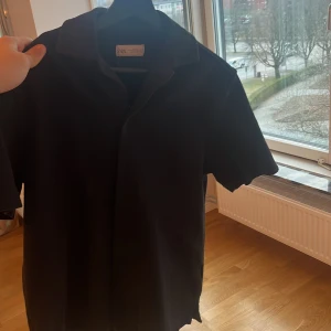 Svart kortärmad skjorta - Snygg svart kortärmad skjorta från Zara med klassisk krage och knappar framtill. Perfekt för en stilren look. Passar bra till både jeans och chinos.