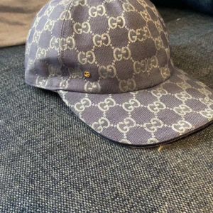 Gucci - Snygg keps från Gucci med det ikoniska GG-mönstret i grått och blått. Kepsen har en justerbar rem baktill för perfekt passform. Perfekt för att ge din outfit en lyxig touch. Strl M