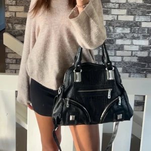 Handväska  - Säljer denna svarta väska med dragkedjor och silverdetaljer. Väskan har lite små skavanker då den blivit använd, bla så har lite av ”skinnet” lossnat, men det är inget man tänker på