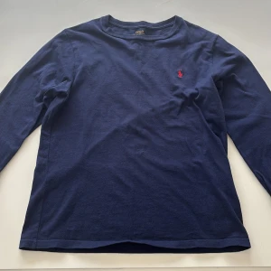 Mörkblå långärmad tröja från Ralph Lauren - Säljer en stilren mörkblå långärmad tröja från Ralph Lauren med det klassiska röda logotypbroderiet på bröstet. Perfekt för en avslappnad och snygg look. Passar bra till jeans. OBS! Det står storlek L på tröjan men den är nertvättad till S eller M 