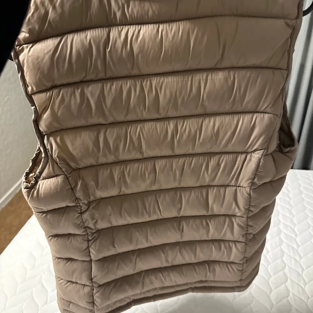 Snygg beige dunväst från Vila med dragkedja framtill. Perfekt för lager-på-lager under kyliga dagar. Västen har en quiltad design och är både stilren och praktisk.. Takit.