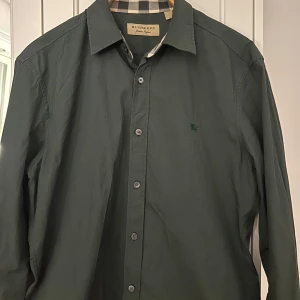 Burberry skjorta - Grön burberry skorta i storlek M man. Använd mycket men helt som ny. Köpt för ungefär 6500 kr. PRIS KAN DISKUTERAS!
