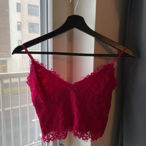Röd spetslinne - Säljer ett snyggt rött spetslinne med smala axelband. Toppen är croppad och har en vacker spetsdesign som ger en romantisk känsla. Perfekt för att piffa upp vilken outfit som helst! Lappen med tvättråd avklippt. 