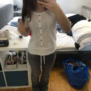 Vit blus från Isolde - Säljer en söt vit blus från Isolde med korta ärmar och fina spetsdetaljer framtill. Blusen har knappar och ett knytband i midjan för en justerbar passform. Perfekt för en somrig look! 🌼