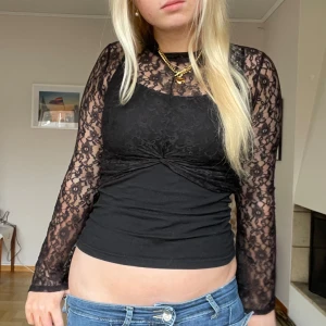 Svart spetsblus - Säljer en snygg svart spetsblus med långa ärmar och en twistdetalj framtill. Perfekt för att ge en elegant touch till din outfit. Blusen är figurnära och har ett vackert mönster i spetsen.