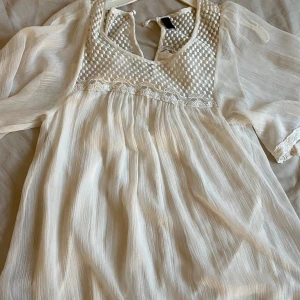 Vit mini klänning  - Vit mini klänning från Vero Moda, fint mönster längst ner och på armarna även mönster över bröstet, Bra skick förutom att där man knäpper på baksidan har gått sönder men går lätt att sy samman(Bild 3) Storlek S 💕