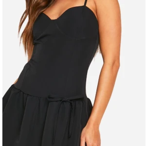 Svart kortklänning med smala axelband - Snygg svart kortklänning med smala axelband och en söt knytning i midjan från boohoo. Perfekt för en kväll ute eller en speciell tillställning. Klänningen har en figurnära passform upptill och en lätt utställd kjol. Aldrig använd. Den är i storlek 40 men skulle säga att den passar mindre också😊