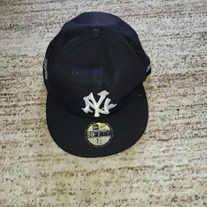 Svart keps från New Era - Snygg svart keps från New Era med broderad logga framtill och World Series-märke på sidan. Kepsen har en platt skärm och MLB-logga baktill. Perfekt för att komplettera din streetwear-look.