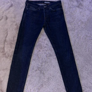 Mörkblå jeans med knappar som gylf. - Snygga mörkblå jeans i slim fit med låg midja. De har knappar framtill och klassiska fem fickor. Byxorna har ingen dragkedja som gylf utan knappar och dom är använda två gånger och är som nya. Dom är i storlek 30/32.