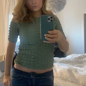 Grön topp med textur - Snygg grön topp med unik textur och korta ärmar. Perfekt för en stilren look. Tillverkad i polyester och elastan för en bekväm passform. Sitter normal i storleken skulle jag säga. Bekvämt material och i nytt skick! Köpt för ca 300kr 