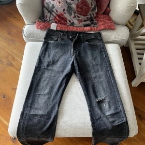 Svarta jeans från Levi's - Snygga svarta Levi's 501 jeans med en klassisk design. De har en rak passform och är tillverkade i slitstarkt denim. Perfekta för en avslappnad stil. Midjemått är W32 och längd L32.