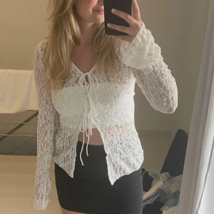 Vit spetsblus med knytning - Säljer en elegant vit spetsblus med knytning framtill. Blusen har långa ärmar och en v-ringad design som ger en romantisk känsla. Perfekt för att lyfta vilken outfit som helst.