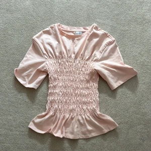Smockad rosa T-shirt  - En snygg ljus rosa smockad T-shirt från other stories, skulle säga att den är väldigt trendig och sjukt snygg till sommarn! Storlek : Xs , aldrig använd!🥰 (obs pris kan diskuteras) FRI FRAKT