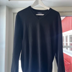 Svart tröja från Crocker - Säljer en stilren svart tröja från Crocker med v-ringad hals. Perfekt för en klassisk look. Tröjan har långa ärmar och är gjord i ett mjukt material.