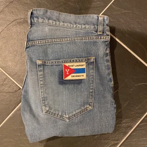 Blå jeans från Saint Laurent - Snygga blå jeans från Saint Laurent med en unik patch på bakfickan. De har en klassisk femficksdesign och en rak passform. Perfekta för en stilren look.