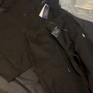 Svarta mjukisbyxor från Polo Ralph Lauren - Svarta mjukisbyxor från Polo Ralph Lauren med dragsko i midjan och klassisk vit logga broderad på benet. Byxorna har en avslappnad passform och är perfekta för en chill stil.