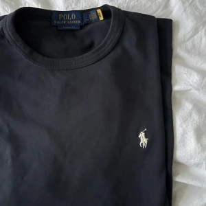 Marinblå t-shirt från Polo Ralph Lauren - Klassisk marinblå t-shirt från Polo Ralph Lauren med rund halsringning och broderad vit logga på bröstet. Enkel och stilren design i mjuk bomull som passar perfekt till sommarens varma dagar 