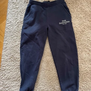 Mörkblå mjukisbyxor / joggingbyxor från Peak Performance - Mörkblå mjukisbyxor från Peak Performance med resår i midjan och fickor på sidorna. Byxorna har logga tryckt på vänster sida och är perfekta för en avslappnad stil. Mjukt material och bekväm passform.