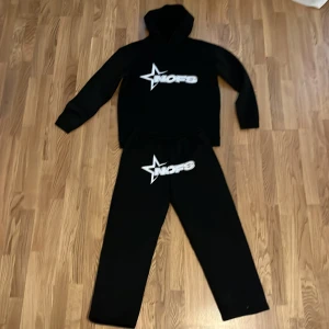 Svart hoodie från NOFS - Svart hoodie med stor vit NOFS-logga och stjärna på bröstet. Klassisk huva och magficka framtill. Perfekt för en avslappnad stil.