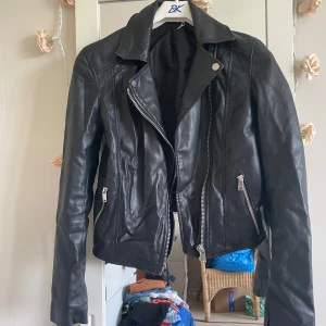 Svart jacka  från H&M Divided - Snygg svart skinnjacka fast den är inte skinn   från H&M Divided med asymmetrisk dragkedja och två fickor med dragkedjor. Fast den är inte i skinn , Klassisk bikerstil med bred krage och långa ärmar. Perfekt för att lyfta vilken outfit som helst.