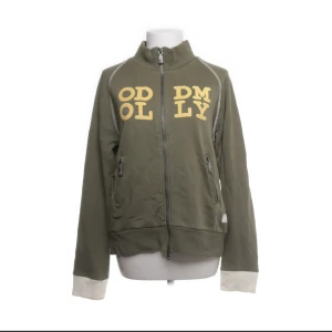 Kofta - Olivgrön jacka med dragkedja från Odd Molly. Jackan har hög krage, vita muddar och tryckt text i gult framtill. Två fickor med dragkedja och ribbade detaljer vid ärmslut och nederkant. Perfekt för en avslappnad stil💚