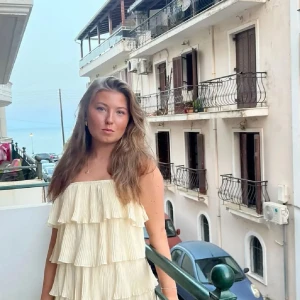 Krämfärgad volangklänning med plisserade lager - Säljer en sät klänning som är plisserad och i en ljusgul färg, superfin nyskick!