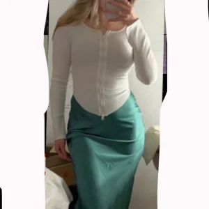 Vit ribbad topp med dragkedj - Säljer en vit ribbad långärmad topp från Nova of Sweden. Toppen har en hel dragkedja framtill och är figurnära med rund halsringning. Sne skuren runt midjan och slits på handleden.