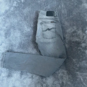 Nudie Jeans Gråa Slim Fit  - Snygga och bekväma Nudie Jeans i modellen Tight Terry (Slim Fit) i storlek W32 L32. Färg: Grå, vilket gör dem enkla att matcha både till vardags och lite mer uppklädda tillfällen. Jeansen är i mycket fint skick och har endast använts varsamt.  🔹 Märke: Nudie Jeans 🔹 Modell: Tight Terry – Slim Fit 🔹 Storlek: W32 L32 🔹 Färg: Grå 🔹 Skick: Mycket fint skick  ⸻  Liknande märken: Levi’s, Acne Studios, Neuw, Dr. Denim, Cheap Monday  Sökord: nudie jeans herr, tight terry jeans, slim fit jeans grå, nudie