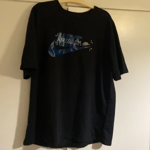 Svart Nike Air Max t-shirt - Svart t-shirt från Nike med blått och vitt Air Max-tryck på bröstet. Klassisk passform och rund halsringning. Perfekt för en sportig och avslappnad stil.