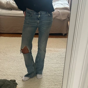 Ljusblå bootcut jeans med hål på knät - Säljer ett par ljusblå jeans med bootcut passform och ett stort hål på ena knät. Jag är 178, midjemått 39, innebenslängd 86