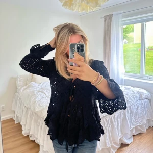 Svart topp - En fin svart topp med volanger och spets liknande blommor i tyget. Storlek M, köpt för 599 kr