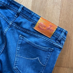 Blå jeans från Jacob Cohen style 688 - Säljer ett par klassiska blå jeans från Jacob Cohen, modell style 688. Jeansen har normal passform, raka ben och knappar i gylfen. Snygga detaljer och läderpatch bak i midjan. Perfekta till vardags och lätta att matcha med det mesta.