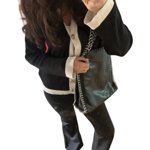 Autentisk Tiamo väska - Säljer en svart axelväska från Tiamo med grov silverfärgad kedja som axelrem. Väskan har en mjuk struktur och dragkedja på insidan. Perfekt för dig som vill ha en stilren accessoar med lite edge. 