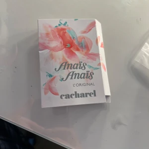 Anaïs Anaïs L'Original Eau de Toilette från Cacharel - Anaïs Anaïs L'Original från Cacharel är en klassisk parfym i en vit kartong med stora rosa och gröna blommor. Förpackningen har en feminin och romantisk design och innehåller en 2ml sprayflaska med doften. 