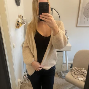 Beige stickad kofta  - Mysig beige stickad kofta med öppen front och långa ärmar från Lindex i storlek M. Koftan har en avslappnad passform och är perfekt att slänga på sig över en topp🩷