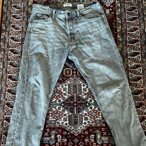 Grå raka jeans från Jack&jones - Grå jeans får j&j med en knappgylf och en liten lagad skada i högra benet som inte syns 