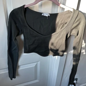 Mörkgrå croppad ribbad topp från Zara - Säljer en mörkgrå croppad topp från Zara med lång ärm och djup v-ringning. Toppen är ribbad och har en tight passform, perfekt att styla med höga jeans eller kjol. Köpte här på Plick men säljer nu då den har blivit för liten! ❤️