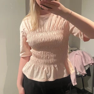 Ljusrosa blus med smock från & Other Stories - Supersöt ljusrosa blus från & other stories med smock över bysten och midjan. Blusen har korta ärmar och volang nertill 🩷
