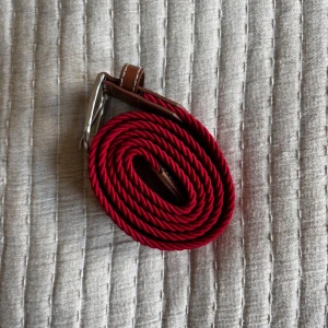 Rött flätat bälte med skinn-detaljer - Säljer ett snyggt rött flätat bälte med bruna skinn-detaljer och silverspänne. Perfekt accessoar för att lyfta din outfit. Bältet har klassisk design och passar till många olika stilar. Hojta till vid frågor🙋‍♂️