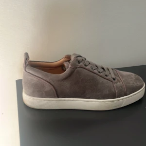 Grå loubs - Snygga grå sneakers i mocka med vit platt sula och den ikoniska röda undersidan. Skorna har rund tå och snörning framtill. Perfekta för dig som vill ha en stilren men ändå unik look.