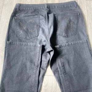 Grå jeansbyxor - Säljer ett par grå jeansbyxor från Mingel Jeans med raka ben och snygga strasstenar på bakfickorna. Klassisk femficksmodell med knapp och dragkedja framtill. Perfekta för dig som vill ha något stilrent men ändå med en twist.