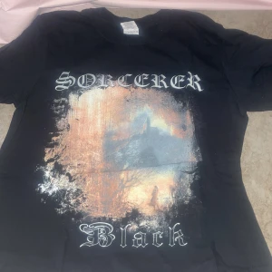Svart band-t-shirt - Cool svart t-shirt med trycket 'Sorcerer Black' och ett stort konstnärligt motiv på framsidan. Klassisk passform och korta ärmar, perfekt för dig som gillar band-merch och streetstyle.