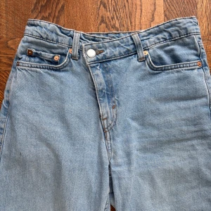 Ljusblå baggy jeans med sne cool knapp - Säljer ett par ljusblå baggy jeans med regular midja och vida. Jeansen är omsydda till utsvängda och har klassiska fem fickor. Knappen där uppe är sne vilket är så cool design. Perfekta för dig som gillar en avslappnad och trendig stil. Storlek 25