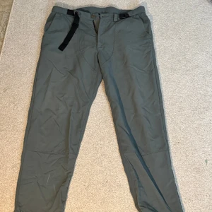 Grå friluftsbyxor med bälte - Säljer ett par grå friluftsbyxor med inbyggt svart bälte och raka ben. Byxorna har förstärkta knän och är perfekta för utomhusaktiviteter. Stängs med knapp och dragkedja framtill.