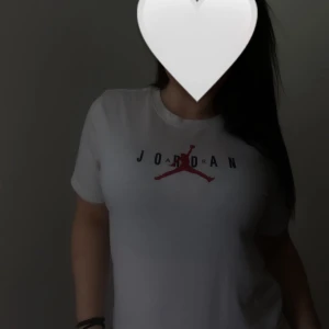 Vit Jordan t-shirt med logga - Säljer en vit t-shirt från Jordan med klassisk logga och text på bröstet. T-shirten har rund halsringning och korta ärmar. Perfekt för en sportig och avslappnad stil.