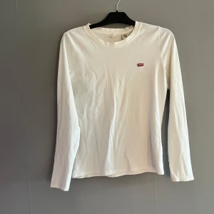 Vit långärmad tröja från Levi's - Säljer en klassisk vit långärmad tröja från Levi's med rund halsringning och liten röd logotyp på bröstet. Tröjan är i mjuk bomull och passar perfekt till jeans eller kjol. Enkel och stilren design. Jag har S och min syster L i storlek och den passar oss båda