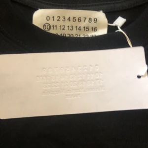 Svart t-shirt från Maison Margiela med tryck - Cool svart t-shirt från Maison Margiela med deras ikoniska siffror och vit splatter-effekt! Kvalitetativt tyg med mycket textur. Riktigt fet helt oanvänd dessutom. Priset är ej bestämt men svarar inte på skambud👌