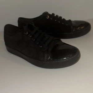 Svarta sneakers från Lanvin - Säljer ett par helsvarta sneakers från Lanvin med snygg kombination av mocka och skinn. Skorna har rund tå, snörning och platt sula. Perfekta för dig som gillar stilrena och klassiska skor med exklusiv känsla.